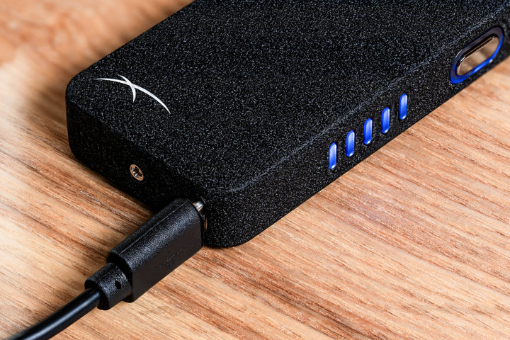 Black Flare lighter lying down on wooden table with LED power bar illuminated and USB charge cord plugged in