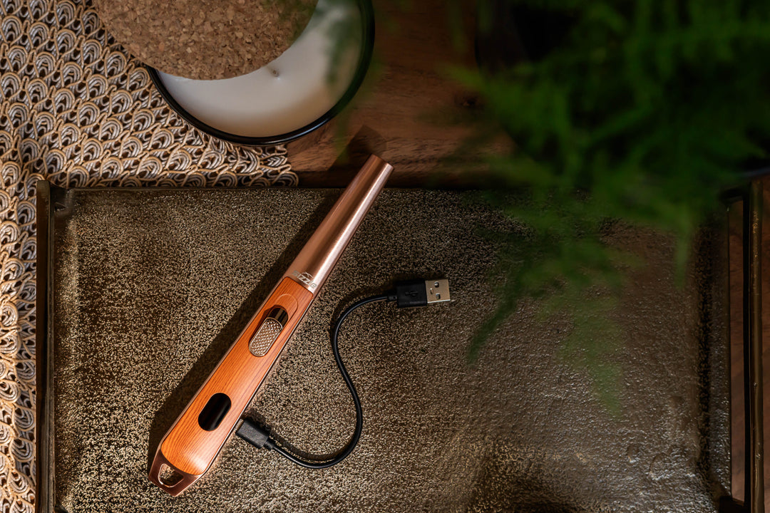 Sizzle LUX USB rechargeable lighter with Oak finish displayed on a brown serving tray with USB charge cord. Green plant. candle in glass.