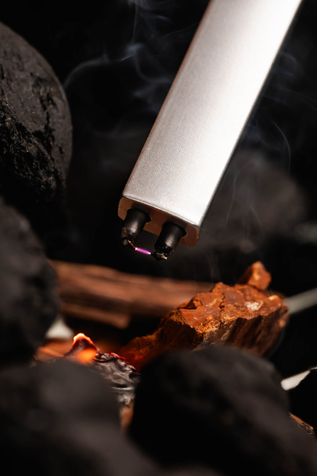 Sizzle Pitmaster USB rechargeable lighter tip displaying the bright plasma arc ignition surrounded by charcoal briquettes 