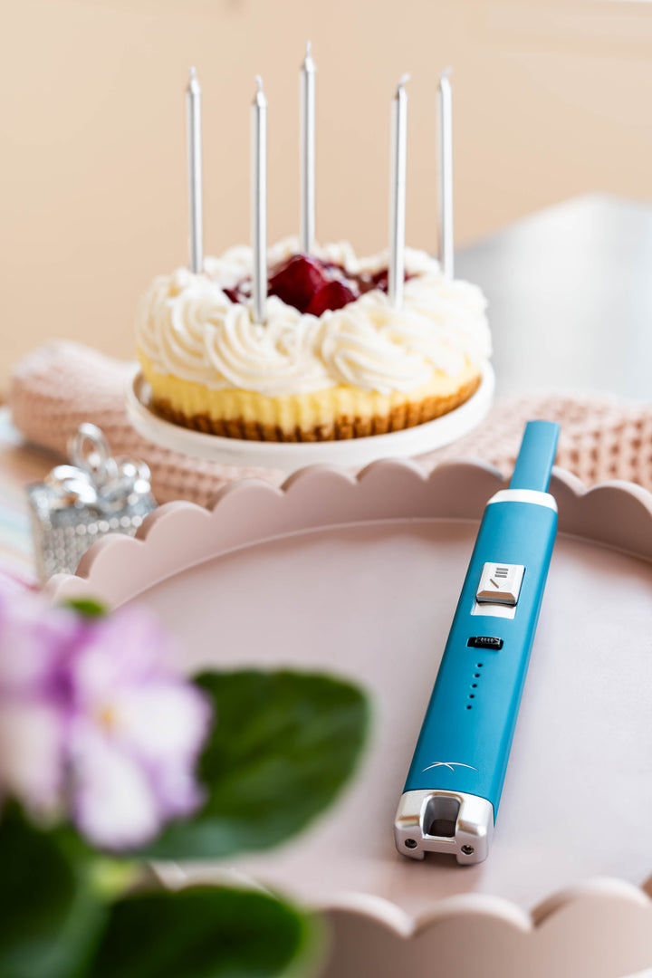 Sizzle Pitmaster USB rechargeable lighter in Teal color beside a strawberry cake with five long silver candles inserted