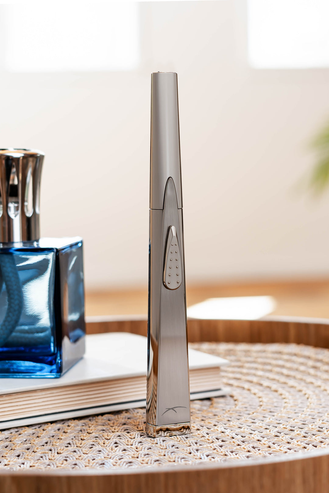 Sizzle Sleek USB rechargeable lighter in silver metal casing standing upright on doily with blue diffuser sitting on a book in the background