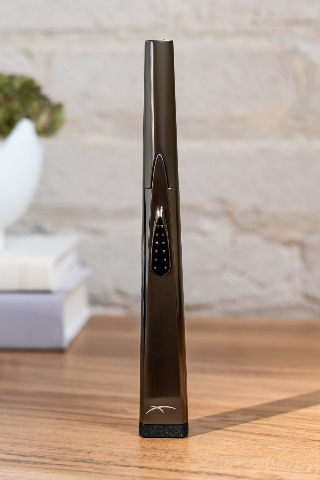 Sizzle Sleek USB rechargeable lighter in pewter metal casing standing upright on a wooden table with plant on books in background