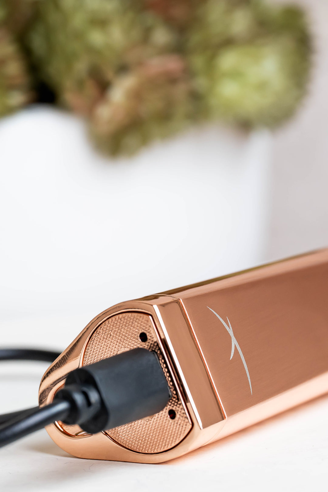 Sizzle Sleek USB rechargeable lighter in rose gold metal casing lying on its side with black USB charge cable inserted