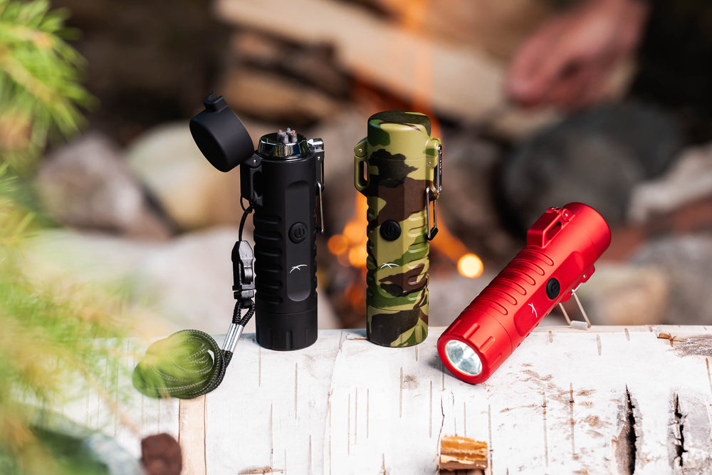 Three (3) Sizzle Survival USB rechargeable lighter/flashlights in black, camouflage and red waterproof casing displayed on a birch log with a fire lit in a fireplace in the background 