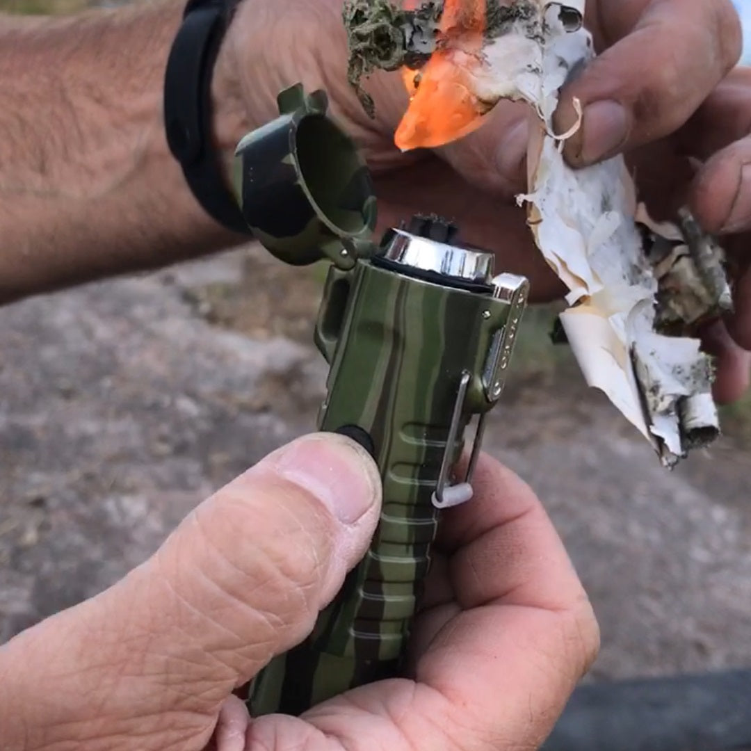A man holding a Sizzle Survival USB rechargeable lighter/flashlight igniting birch bark