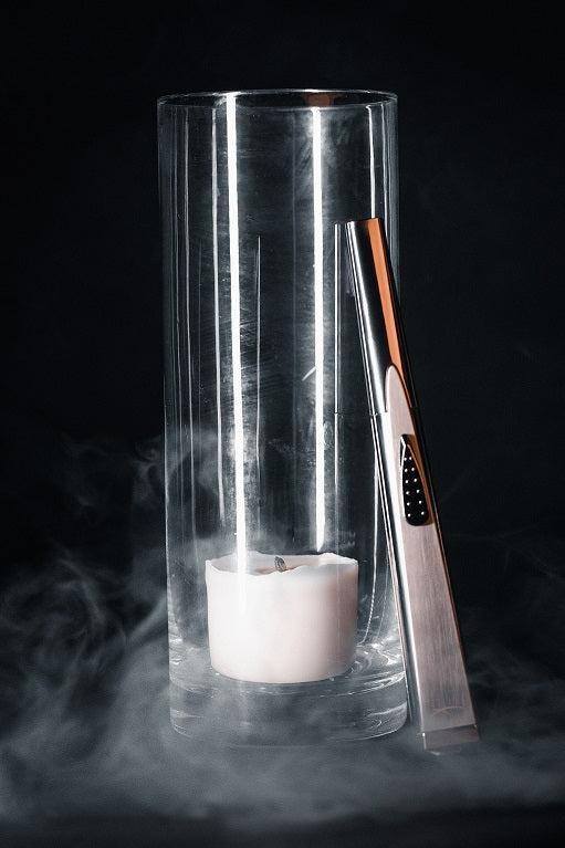 Sizzle Sleek USB rechargeable lighter in silver metal casing leaning on a deep vase with a candle shrouded in light smoke.