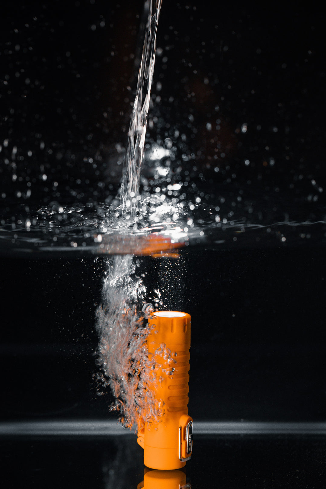 Sizzle Survival USB rechargeable lighter/flashlight in orange waterproof casing submerged underwater with water pouring down with flashlight illuminated